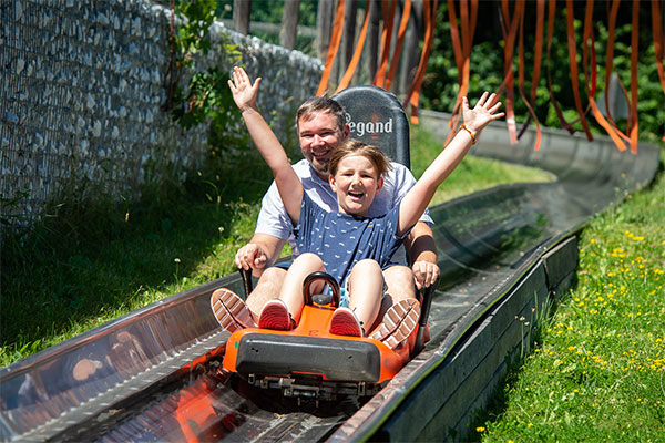 Vater und Kinder fahren mit der Sommerrodelbahn talwärts