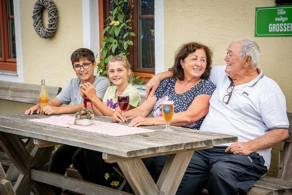 Oma und Opa sitzen mit Enkelin und Enkel auf der Terrasse und haben ein Getränk bestellt.