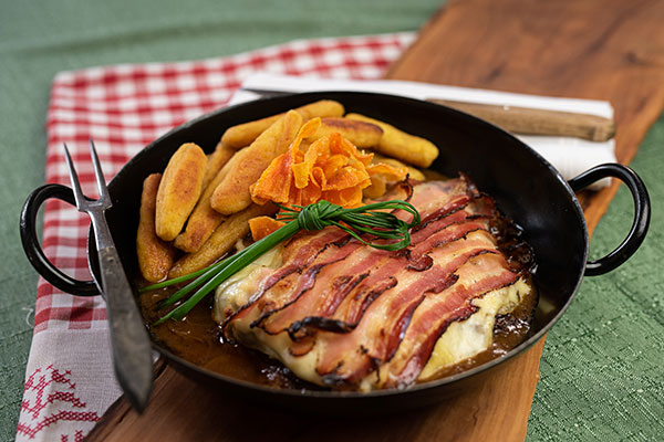 Speise im Pfandl angerichtet - Fleisch überbacken mit Speck und Käse und daneben Schupfnudeln.
