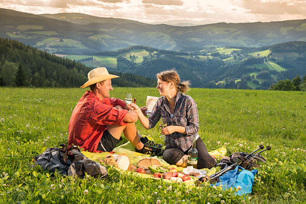 Pärchen sitzt auf grüner Wiese und mach ein Picknick.