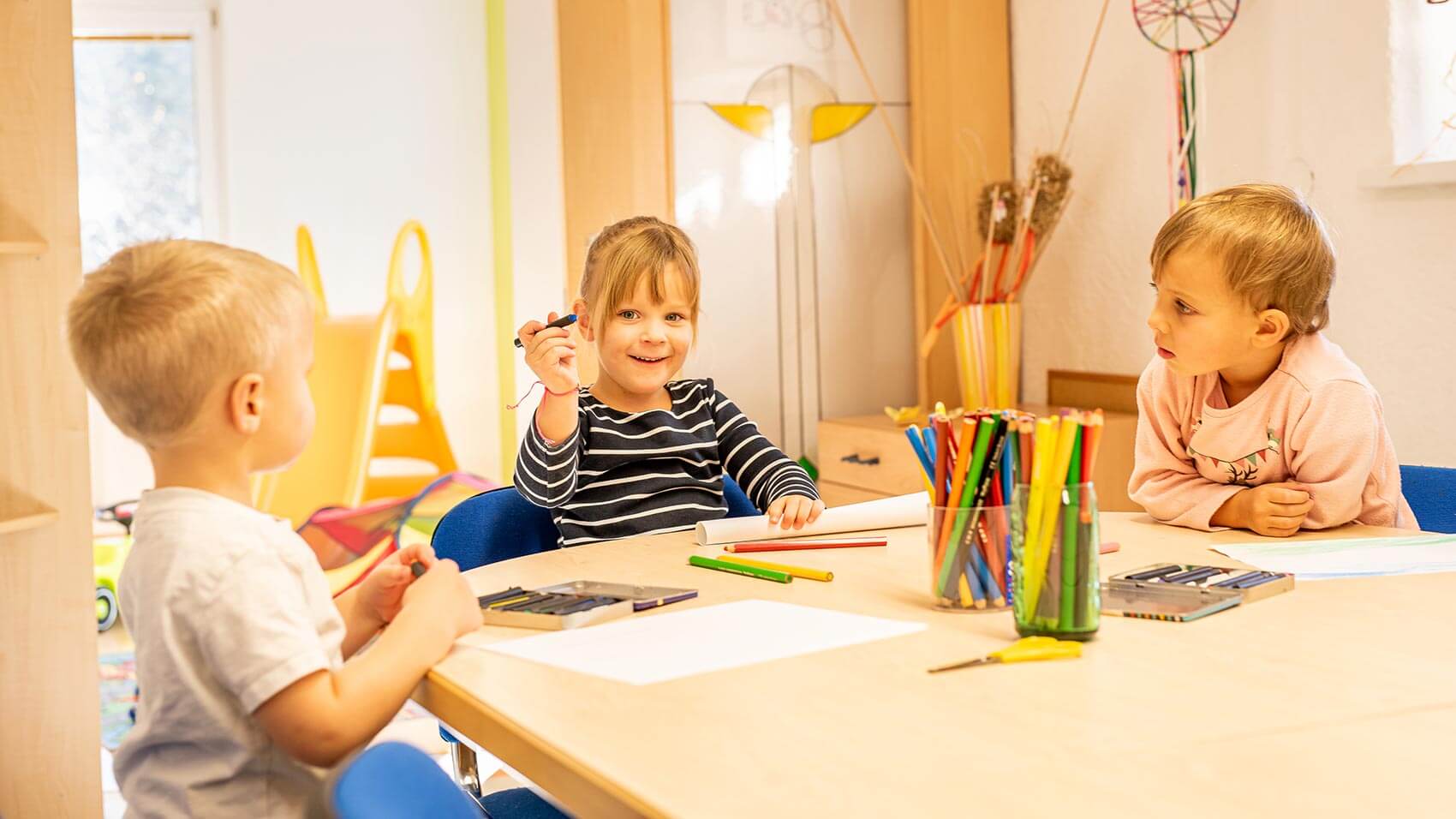 Drei Kinder am runden Tisch sitzend mit Buntstifte und Papier