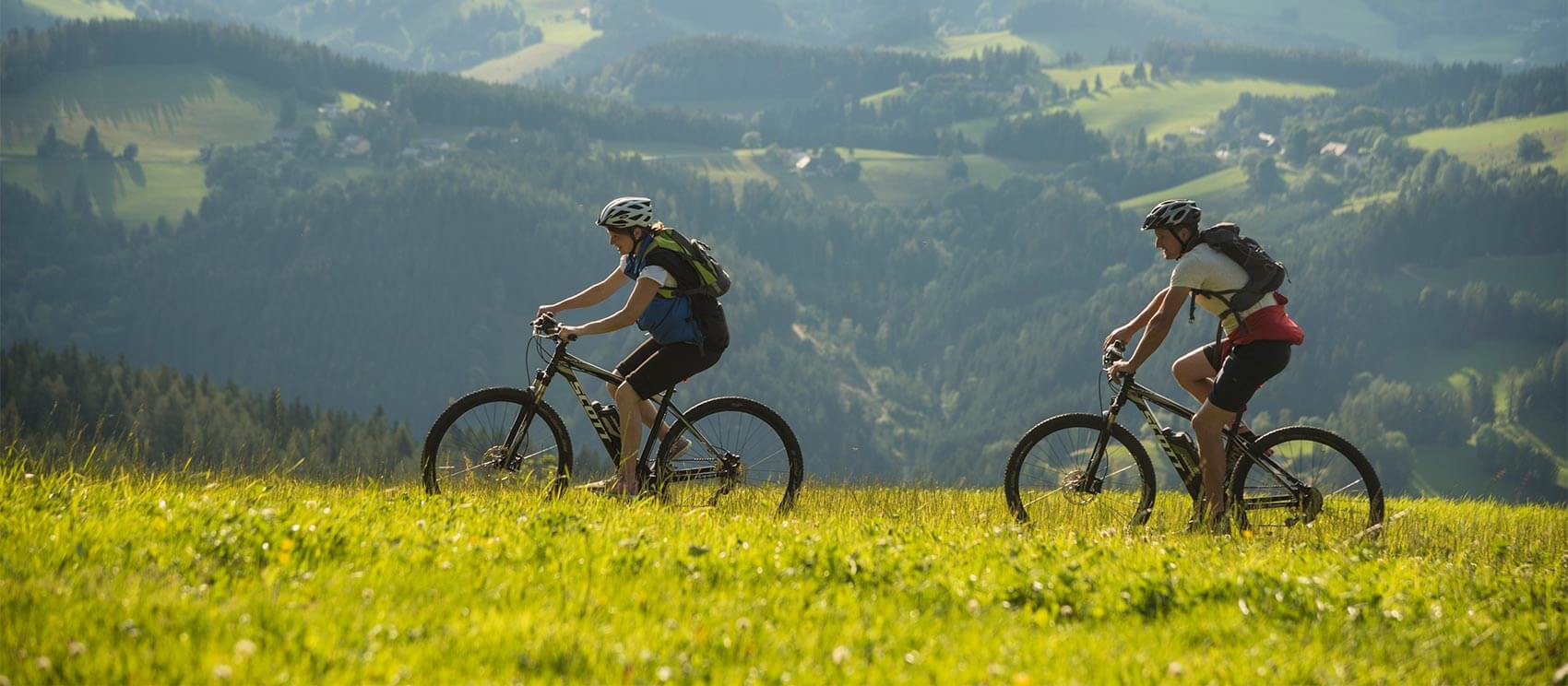 Zwei Mountainbiker unterwegs auf eine schmalen Weg durch eine saftig grüne Wiese