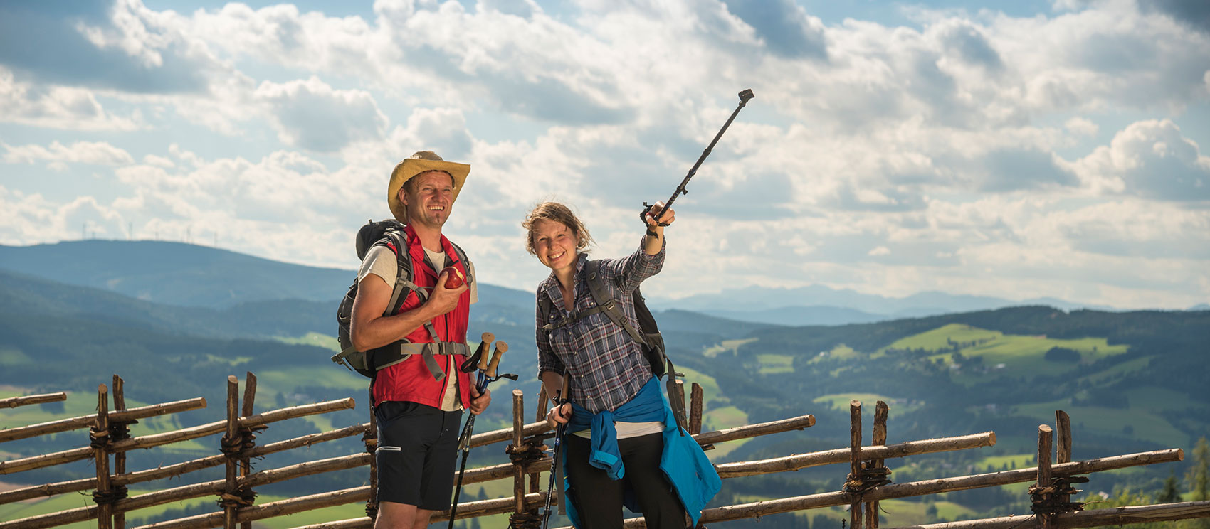 Wanderpärchen mit Rucksack und Nordic-Walking-Stöcken ausgestattet blickt mit Freude in die Landschaft
