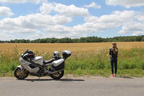 Frau, die den Rücken zudreht und in die Landschaft schaut - daneben steht ein Motorrad.